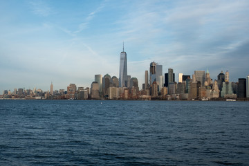 Famous New York City skyline and New York Harbor as seen from a boat.  Blue skies and cirrus clouds over New York's Financial district.  Sunny day looking at Manhattan from the water.