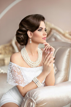 Retro woman portrait. Elegant brunette lady with fashion pearls jewelry set, french manicure nails, wavy hairstyle and makeup. Gorgeous model posing on luxury armchair  in modern interior.