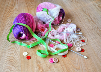 Skeins of thread, buttons and measuring tape on wooden background.