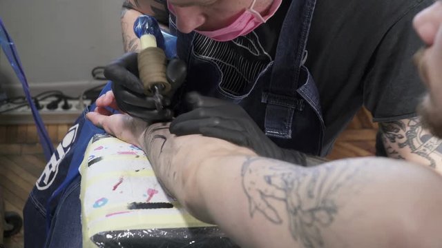 A tatooer coloring tatoo on man's hand