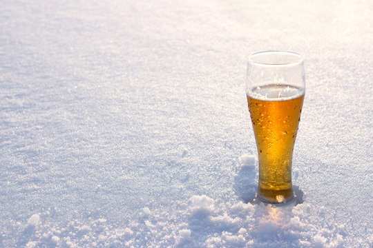 Mug of cold beer in the snow at sunset. Beautiful winter background. Outdoor recreation. Advertising of alcoholic beverage. Booze and holidays.