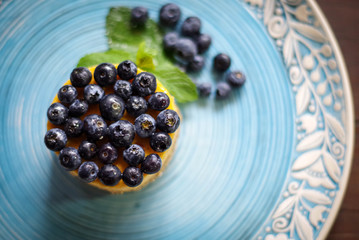 Very gentle blueberry dessert with fresh blueberries and white curd cream and shortcake dough and green mint on a blue plate.
