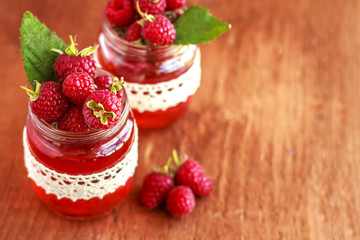 Rustic fresh ripe raspberry in glass bottle with leaves on brown background. Copy space. Close up. Top view.