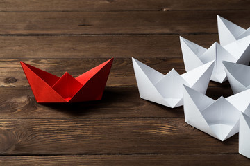Business leadership concept with white and color paper boats on wooden table