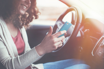 Smiling curly woman sitting in non moving car and using her mobile phone