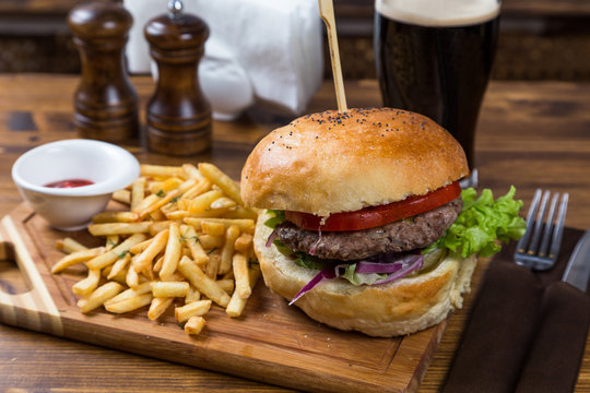 hot burger serving on wooden board with dark beer