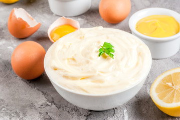 Mayonnaise with ingredients for cooking - eggs, vegetable oil, mustard, lemon, parsley. On the grey stone concrete table close view copy space
