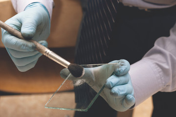 Police forensic expert taking fingerprints from the glass with a special brush. The investigation...