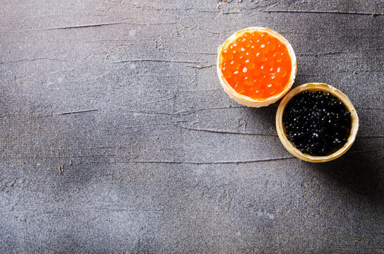 Black and red caviar tartlets, appetizer canapes on gray background, top view