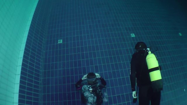 Two girls diver in scuba gear swimming along the pool, top view.
