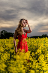 Naklejka na ściany i meble Woman in a red dress in a yellow raapseed field with beautiful sunset and sky