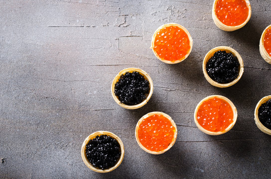 Black and red caviar tartlets, appetizer canapes on gray background, top view