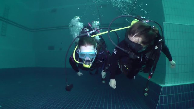 Two girls diver in scuba gear swimming using only one aqualung for breathing.
