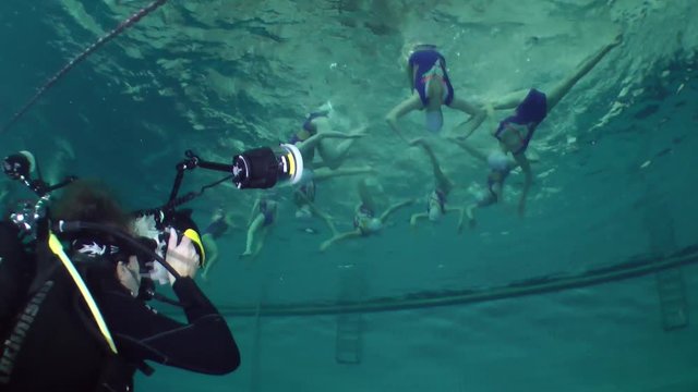 Underwater photographer shooting team of sportswomen in synchronized swimming, wide shot.
