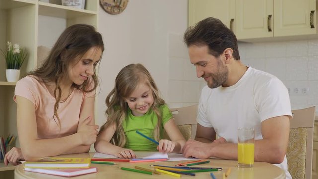 Girl drawing pictures, looking at parents with love, enjoying leisure together