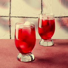 Cold cherry drink with ice cubes in glasses, on pink background