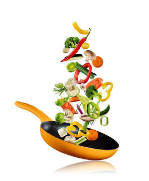 Fresh vegetables flying into a pan on white background