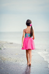 Young girl walking on sandy beach, looking at sea 