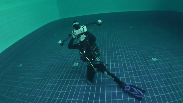 Underwater photographer shoots in the pool, medium shot.
