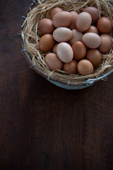 Vertical Top View of Fresh Farm Chicken Eggs in Metal Wire Basket with Raffia on a Dark Brown Wooden Table