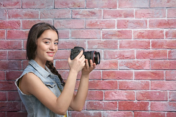 Beautiful young photographer near brick wall