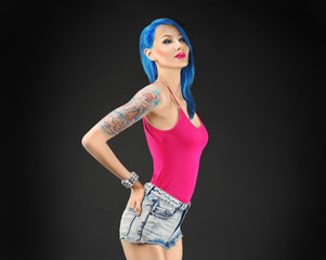 Beautiful young woman with stylish color hair and tattoo on dark background