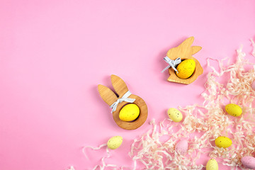 Wooden figures with colourful eggs on pink background