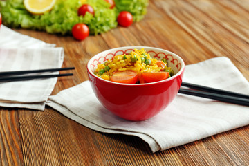 Delicious rice with vegetables in a bowl on wooden table