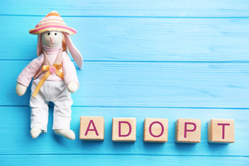 Bunny toy and cubes with word ADOPT on wooden background