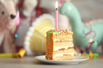 Slice of birthday cake with candle on toys background