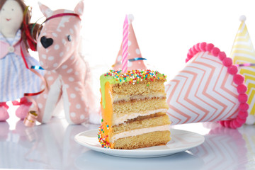 Slice of birthday cake with party hats and toys on white background