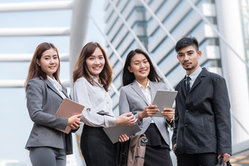 Team portrait of young confident and successful Asian business people smiling outdoor with cityscape in background
