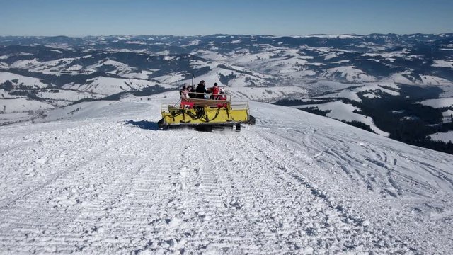 Skiers Riding on the Back of a Snowcat on a Snow Covered Mountain at a Winter Sunny Day