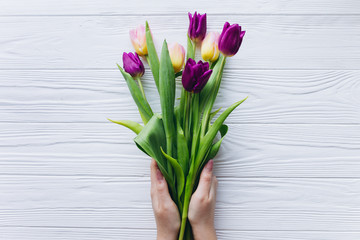 Female holding bouquet with tulips on white wooden background.