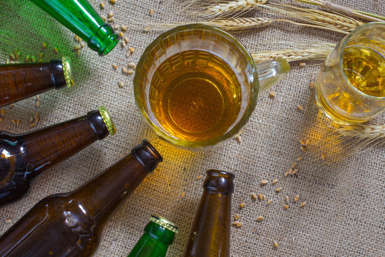 Glass mug of beer. Spikelets of wheat on sacking. Glass bottles