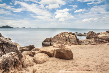 Sandy tropical beach with big round stones and blue sky
