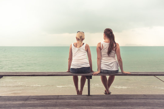 Two young women sitting together and looking into the distance on beach. Concept for togetherness