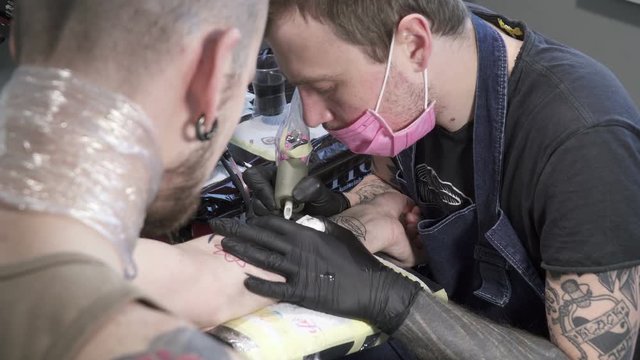 Tatooer in mask and black gloves is making tatoo of insect on hand