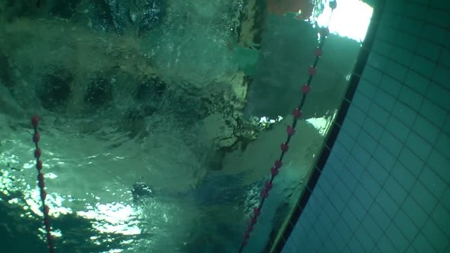 The girl-swimmer starts jumping from pool board, wide shot, underwater view.
