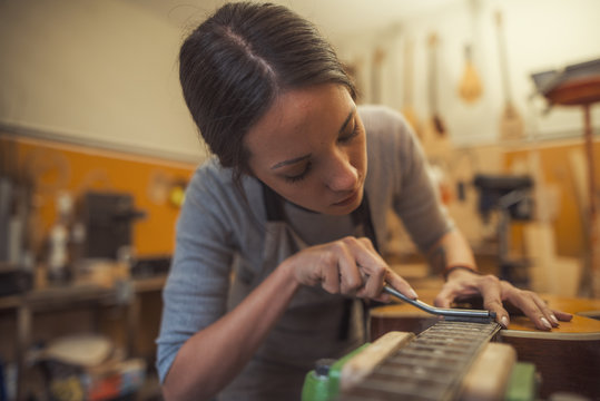 woman luthier is using a tool to grind a classic guitar fretboard in her musical instrument workshop