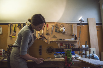 woman luthier is repairing a guitar in her musical instrument workshop - obrazy, fototapety, plakaty