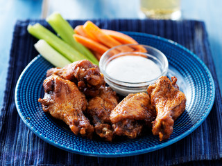 bbq buffalo chicken wings on blue plate with ranch dip and celery sticks
