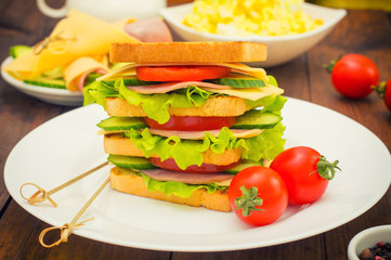 Big sandwich, meat, lettuce, cheese and vegetables on toasted. Wooden background. Close-up