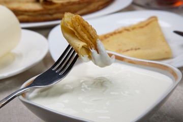 Piece of pancake in sour cream on a fork.