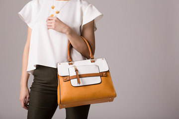 Stylish woman in modern clothes with bright orange white handbag in hands posing at studio isolated on gray background