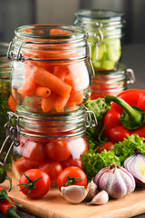 Jars with marinated food and raw vegetables on cutting board