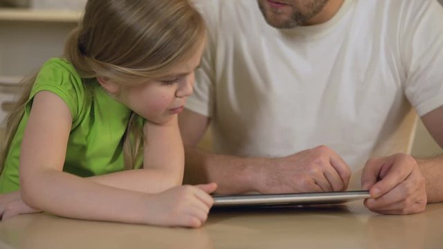 Father showing daughter funny gaming application on tablet, playing together