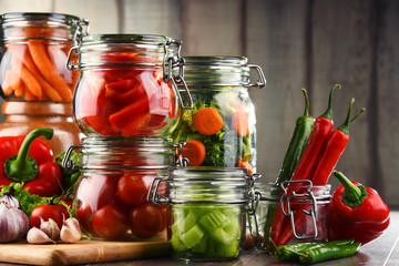 Jars with marinated food and raw vegetables on cutting board