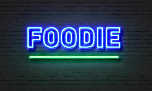 Foodie neon sign on brick wall background.