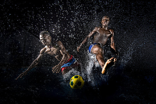 Men playing soccer in water against black background